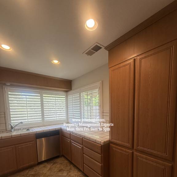 a kitchen with wooden cabinets and a window with blinds.